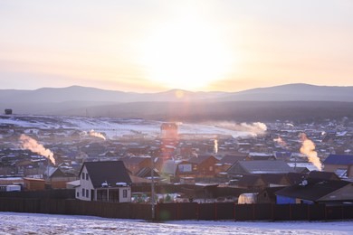 early morning, sunrise in khuzhir village, olkhon island, lake baikal. smoke from home chimneys. rays of light. winter time.