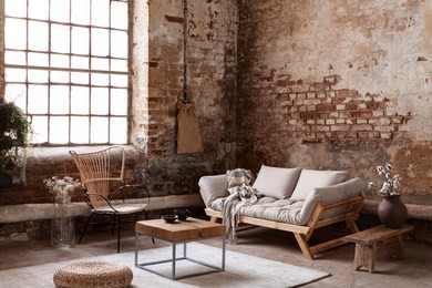 armchair and beige sofa in industrial living room interior with wooden table, pouf and window. real photo