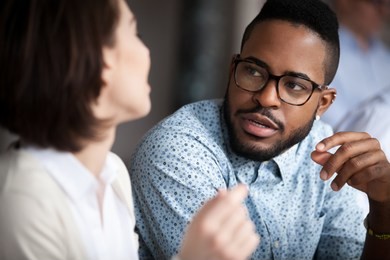 close up of multiracial colleagues chat talking or discussing something in office, black man speak with female coworker negotiating about business project, having conversation. cooperation concept