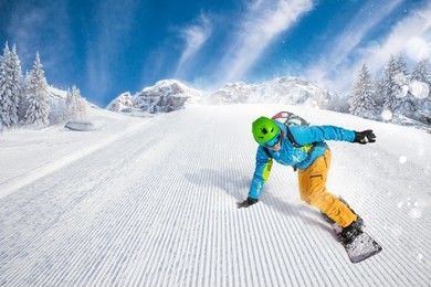 active man snowboarder riding on slope during beautiful sunny day in the ountains.