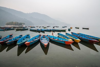 colourful boats at shore of beautiful phewa lake with misty landscape on background. pokhara, nepal