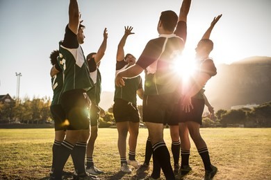 rugby players celebrating a win at the sports field. rugby team with hands raised and screaming after victory.