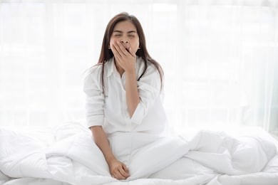 asian woman beautiful young smiling woman sitting on bed and stretching in the morning at bedroom after waking up in her bed fully rested and open the curtains in the morning to get fresh air.