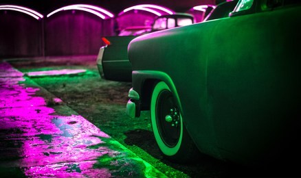 classic american cars are bathed in colorful neon lights. 