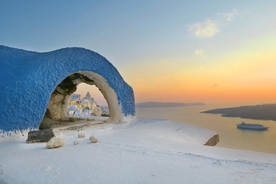 beautiful peaceful magnificent sunset on a greek island of santorini, town of fira, with calm blue sea , a cruise liner in the distance , amazing colors sky and a small part of a town in an arch