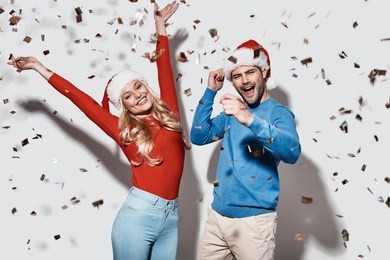christmas party. beautiful young couple in christmas hats gesturing and smiling while standing against grey background