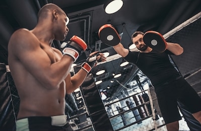 afro american boxer in gloves is training with a coach in the boxing ring
