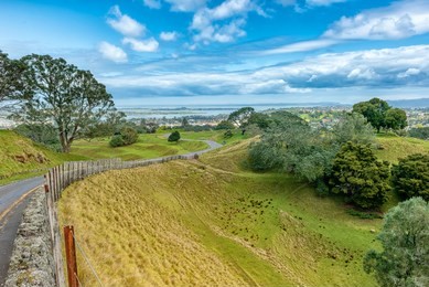 road leading to the summit of one tree hill along the edge of the volcanic cone with the ocean in the distance in auckland new zealand