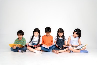 a group of cute little asian boy and girl reading book while sitting or lying over white background