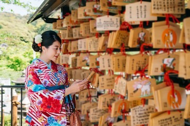 japanese lady looking at letter on wooden board hanging on the praying wall in japanese temple. japanese blessing culture. curious young girl reading others praying card in kiyomizu dera in kyoto.