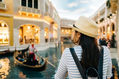 back view of beautiful lady standing beside the river and watching worker sailing the boat in venice. backpacker independent travel in europe. elegant woman enjoy the beauty of the river.