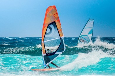 water sports: windsurfers with colored sails in oceanic blue water