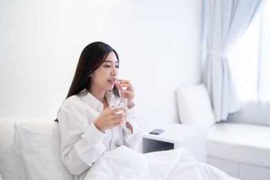 young thai girl business woman taking medicine and drinking water,holding pills,glass of water on bed in hospital bedroom,she work hard while feels sick,drug remedy,health care medical people concept
