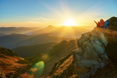 people meeting sunrise in mountains. group of people walking toward mountain summit with backpacks hiking trekking gear meeting uprising sun sunbeams of background.  