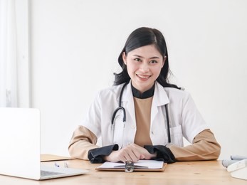 female asian doctor working at office desk and smiling at camera.