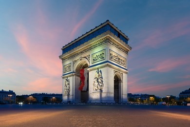arc de triomphe paris and champs elysees with a large france flag flying under the arch in europe victory day at paris, france.