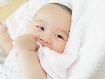 portrait of newborn chinese baby child relaxing in towel after bath or shower. looking and smiling with fingers in mouth, textile and bedding for kids.
