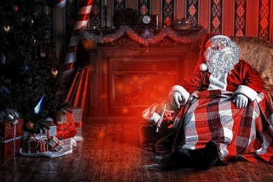 santa claus having a rest in a comfortable chair near the fireplace at home.