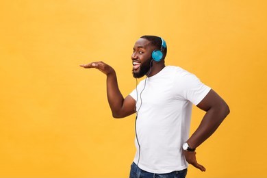 young african american man wearing headphone and enjoy music dancing over yellow gold background