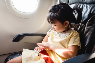 adorable little asian girl traveling by an airplane and fastening seat belt.child sitting by aircraft near window.passenger kid while sitting on the airplane for safe flight.safety travel on holidays.