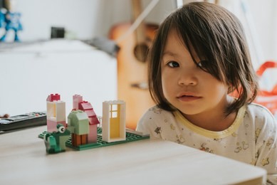 a girl in white yellow pajamas playing lego blocks toy in the morning by herself