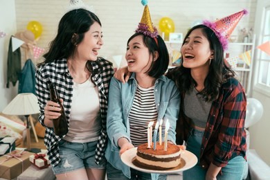 girl best friends birthday party at home. three friends celebrating birthday with surprise in house. female people holding cake with candles on fire smile cheerfully.