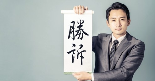 young asian businessman showing a white scroll. / japanese transration: "win a case"