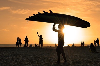 kuta beach in bali at sunset with man carrying surfboards