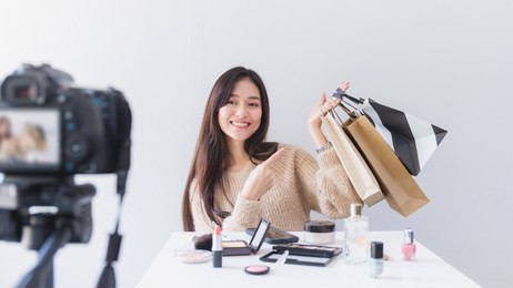 asian beautiful women blogger are using the camera live streaming online with a shopping bag in the white room with cosmetics on table.concept of online shopping business.