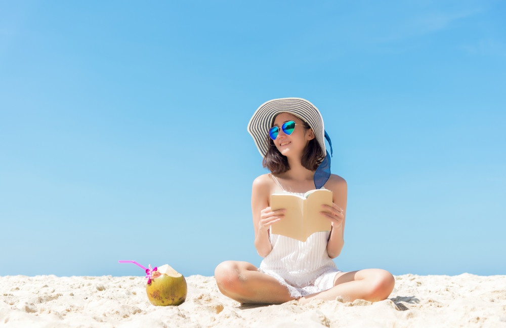 summer vacation. smelling asian women relaxing and reading book on the beach, so happy and luxury in holiday summer, blue sky background. travel and lifestyle concept.
