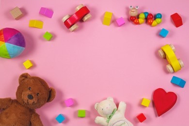 baby kids toys frame with teddy bear, wooden toy car, colorful bricks on pink background. top view