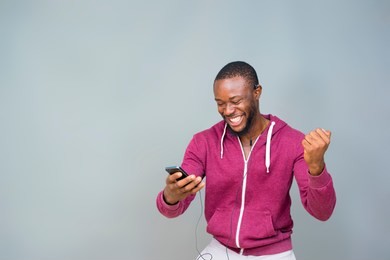 young black man happy and excited and celebrating while looking at his mobile phone 
