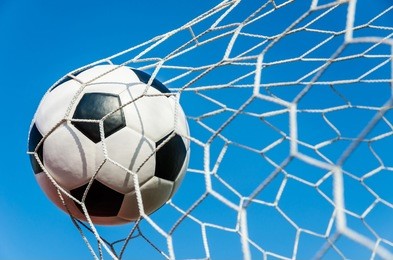 soccer football in goal net with sky field.