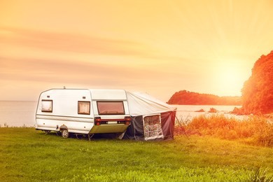 trailer motor home and a tent on the grassy part of the beach at sunset. leisure mobile camping home for tourists overlooking the blue sea and cape. adventure relaxing travel on caravan van