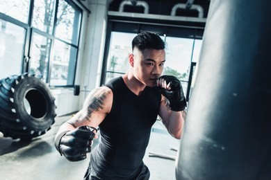 young sportsman wearing boxing gloves and punching boxing bag at gym
