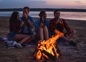 camp on the beach. group of young friends having picnic with bonfire. they drink beer