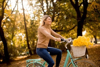 happy active woman riding bicycle in golden autumn park