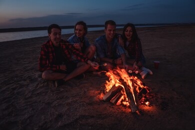 camp on the beach. group of young friends having picnic with bonfire. they eat marshmallows