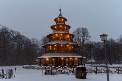 cold winter scene of the empty beer garden around the illuminated chinese tower at the southern part of the englischer garten while snowing heavily in munich, germany.