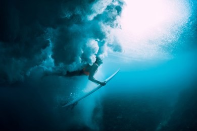 surfer woman with surfboard dive underwater with under big wave.
