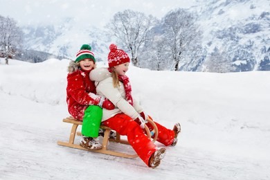 little girl and boy enjoying sleigh ride. child sledding. toddler kid riding a sledge. children play outdoors in snow. kids sled in snowy park in winter. outdoor fun for family christmas vacation.