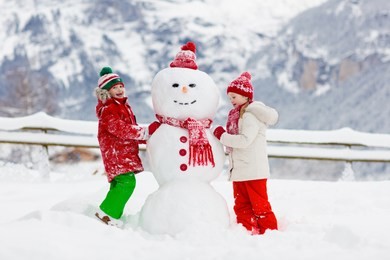 child building snowman. kids build snow man. boy and girl playing outdoors on snowy winter day. outdoor family fun on christmas vacation in the mountains. children play in swiss mountain landscape.