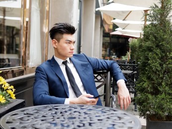 portrait of a handsome businessman in blue suit sitting in a restaurant outdoor, close up upper body view. attractive male hipster chinese model.