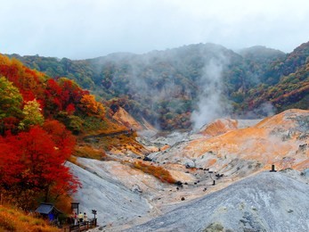 tourists on a wooden terrace admire the awesome barren wasteland with volcanic activities (hot steam vents, sulfurous streams) in autumn season in jigokudani (hell valley) noboribetsu, hokkaido, japan