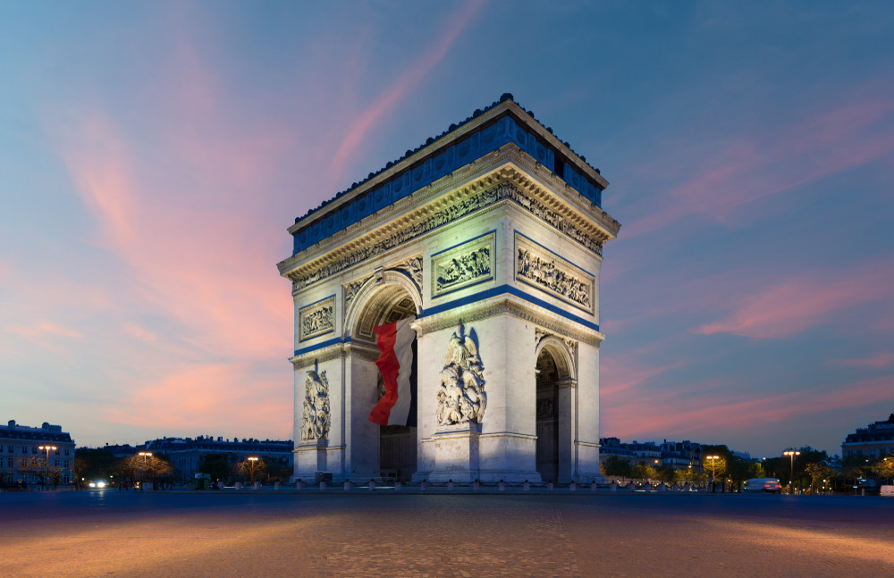 arc de triomphe paris and champs elysees with a large france flag flying under the arch in europe victory day at paris, france.