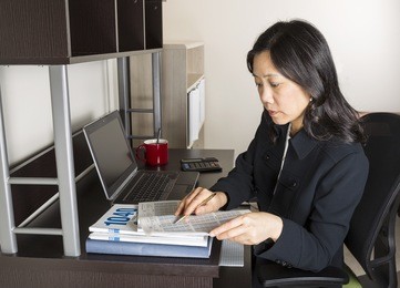 professional mature asian woman  doing income taxes with tax form booklet, calculator, coffee cup and computer on desk