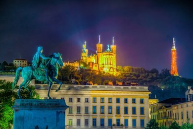 night view of basilica notre-dame de fourviere viewed behind statue of louis xiv in lyon, france
