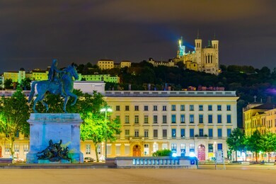 night view of basilica notre-dame de fourviere viewed behind statue of louis xiv in lyon, france