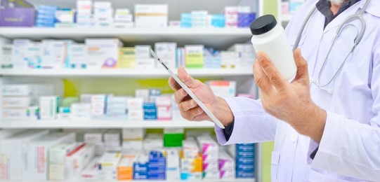 pharmacist holding medicine bottle and computer tablet for filling prescription in pharmacy drugstore.