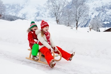 little girl and boy enjoying sleigh ride. child sledding. toddler kid riding a sledge. children play outdoors in snow. kids sled in snowy park in winter. outdoor fun for family christmas vacation.